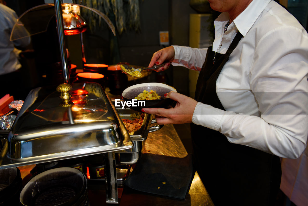 Black bowl with noodles served at a party by a waiter with a black kitchen apron