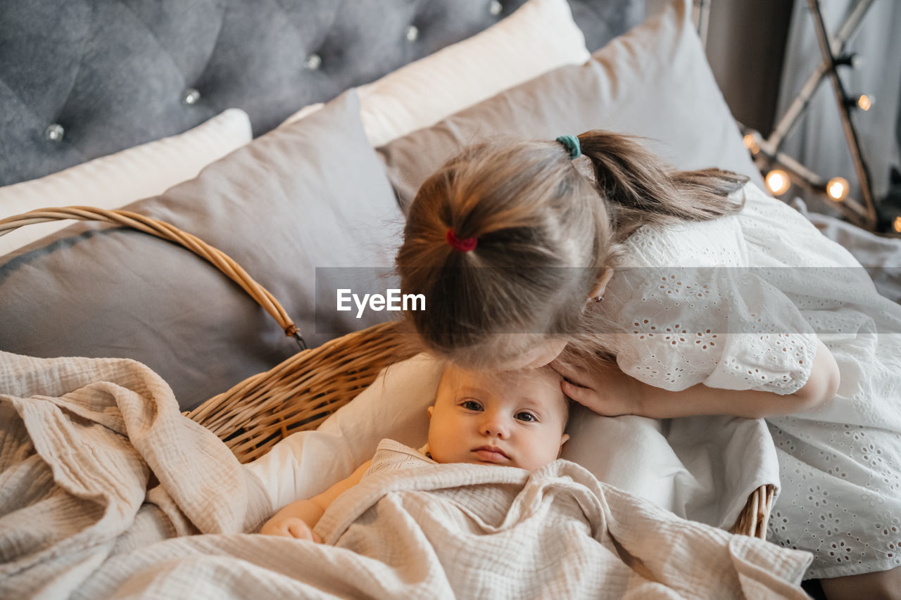 Girl taking care of her younger sister on the bed wicker basket hugs