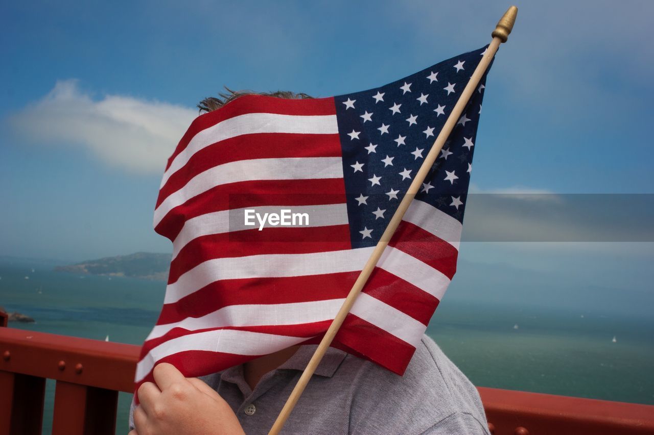 Person face covered with amercian flag against sea