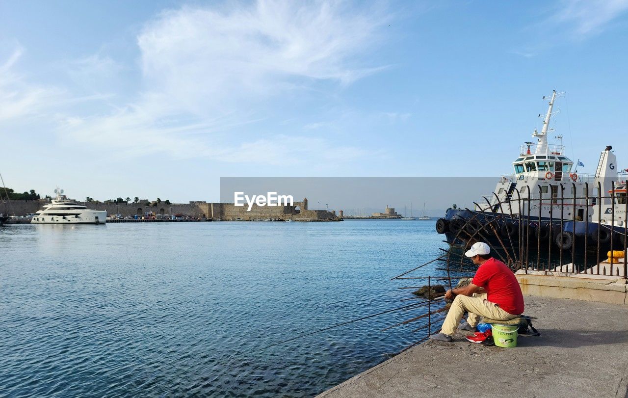 rear view of woman sitting on pier over river against sky