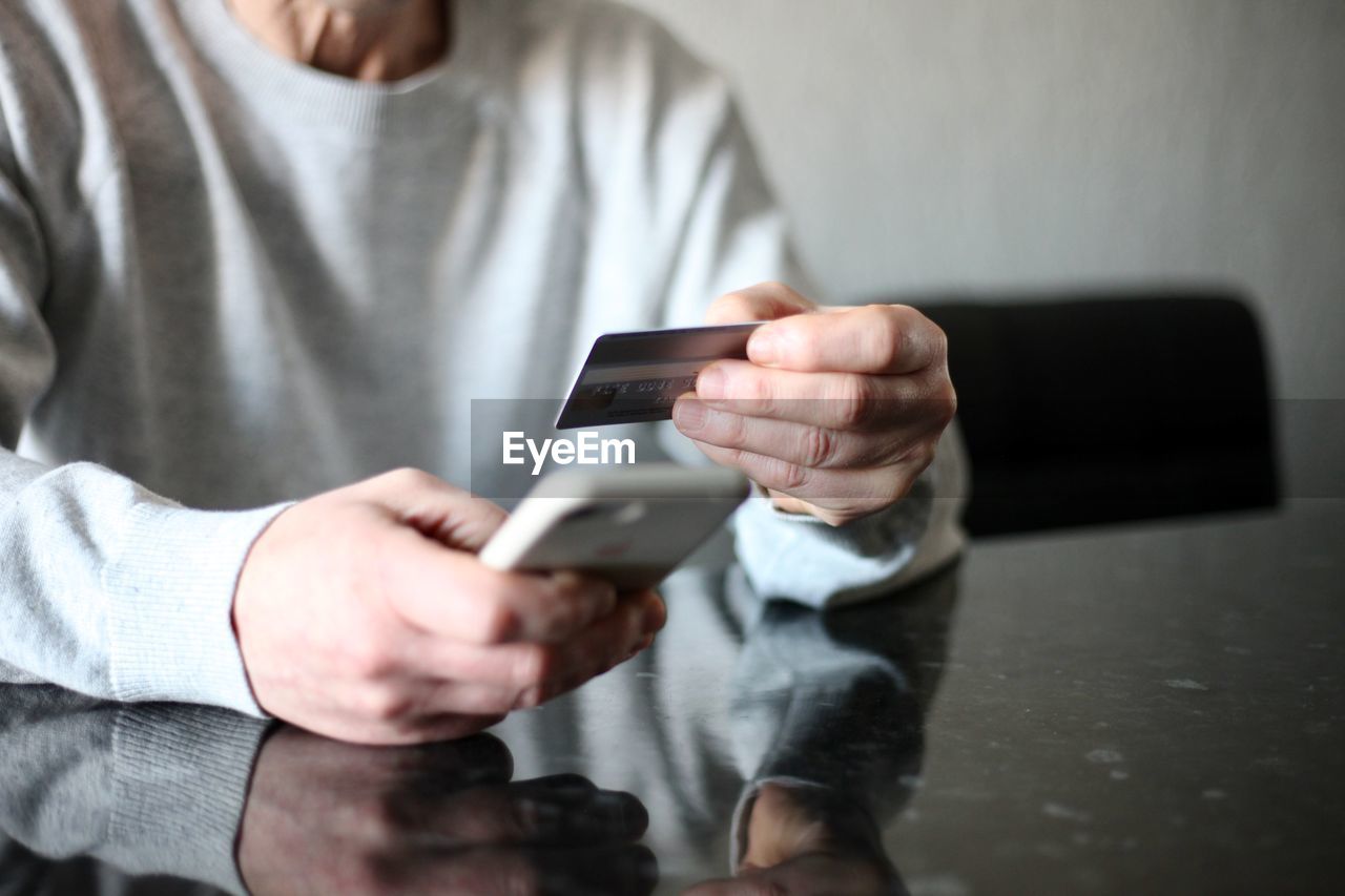 MIDSECTION OF MAN USING SMART PHONE IN LAPTOP