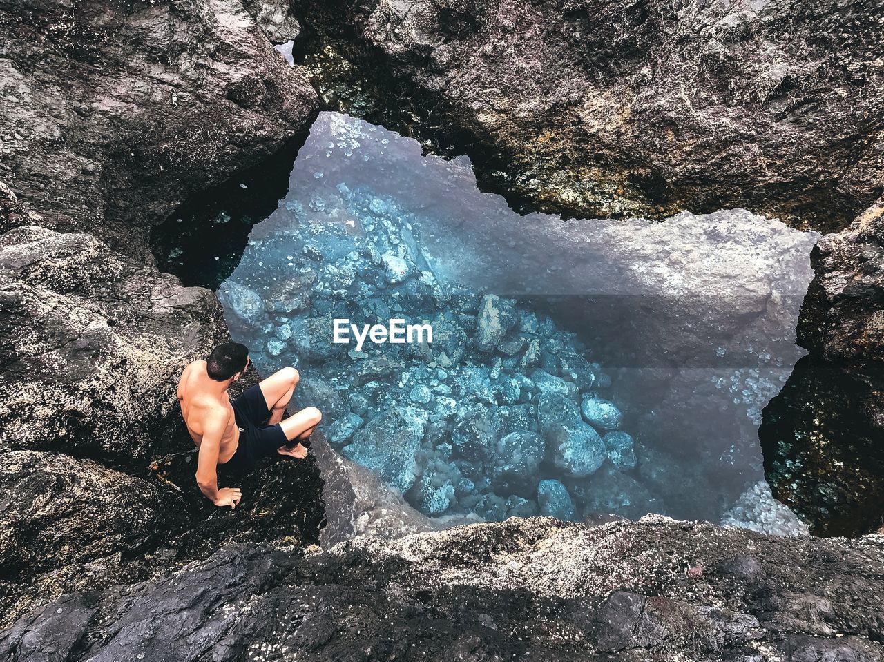 High angle view of shirtless man on rock by pond