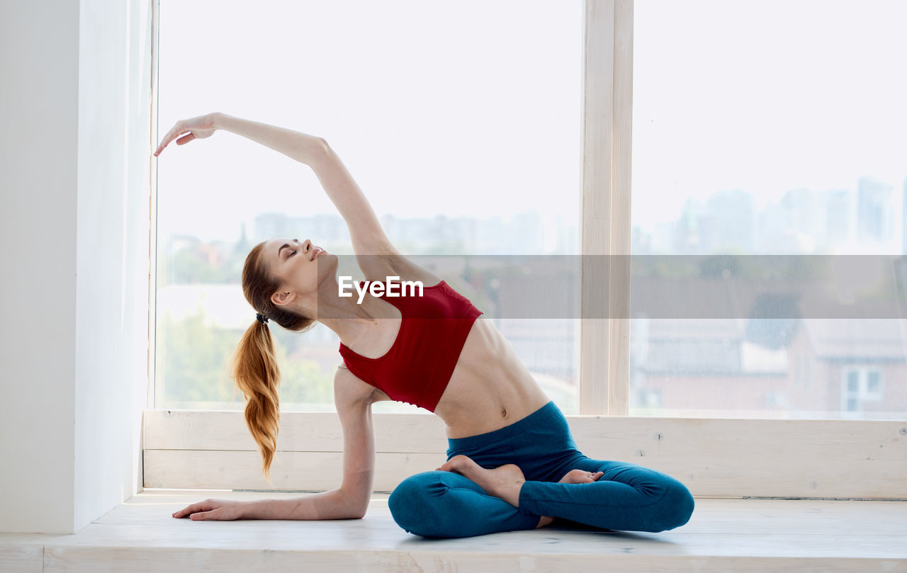 Young woman with arms raised while standing against window