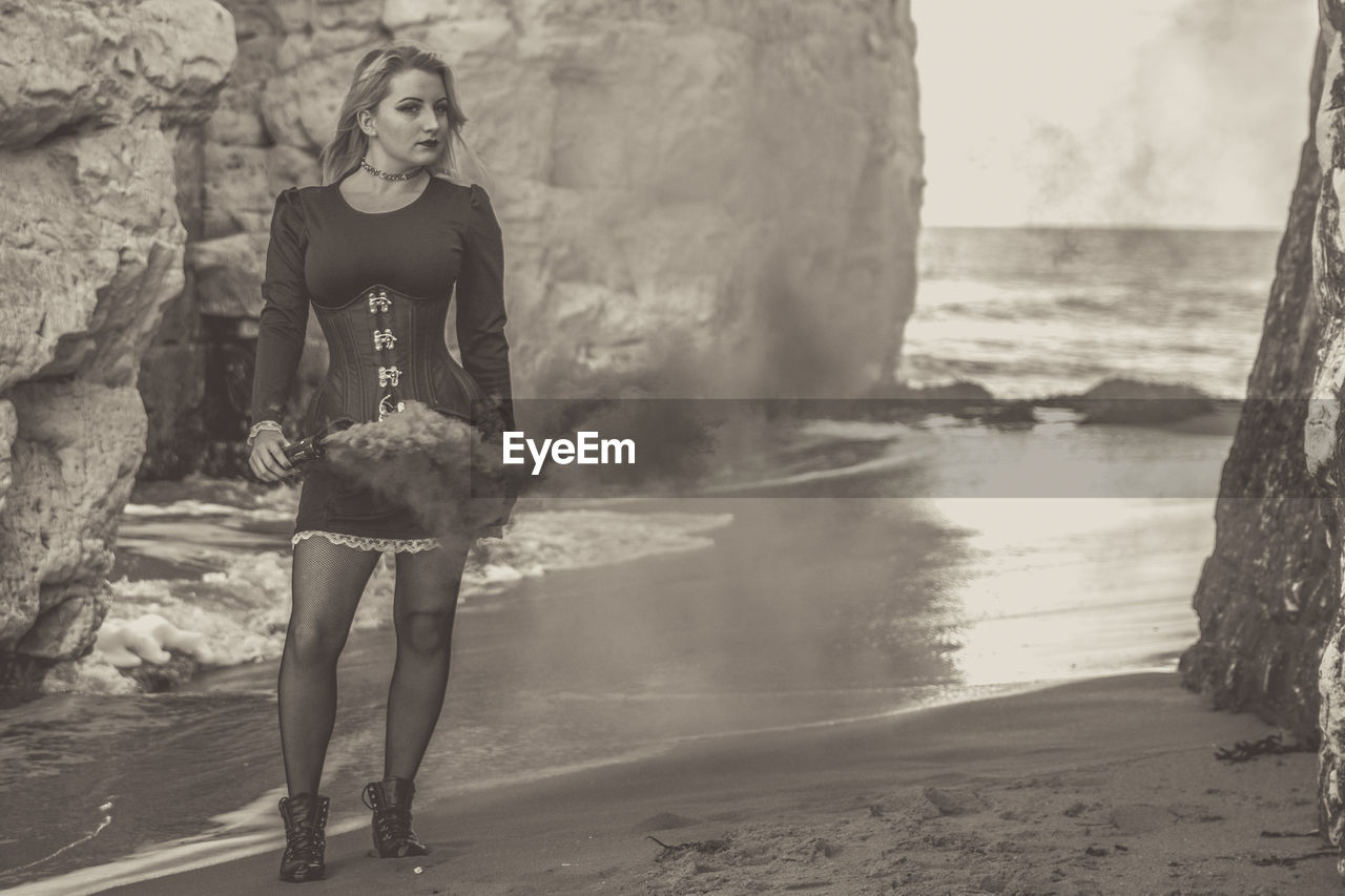 Portrait of young woman with distress flare standing by rock formations at beach