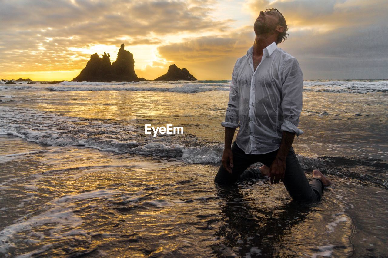 Scenic view of man in sea against cloudy sky at sunset