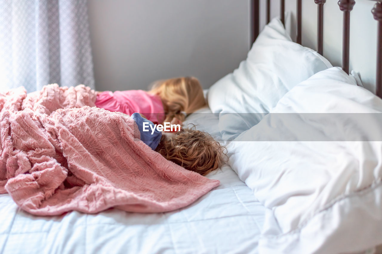 High angle view of cute kids sleeping on bed