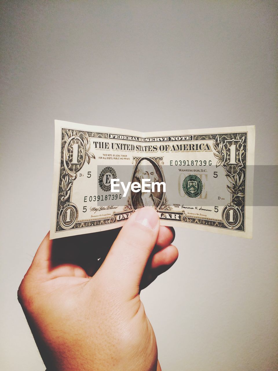 Close-up of hand holding dollar note over gray background