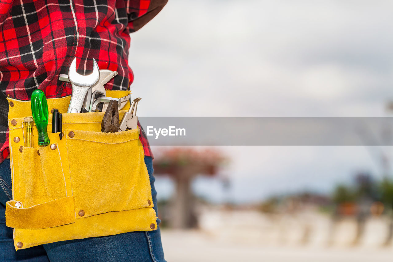 Midsection of man wearing tool belt while standing against sky