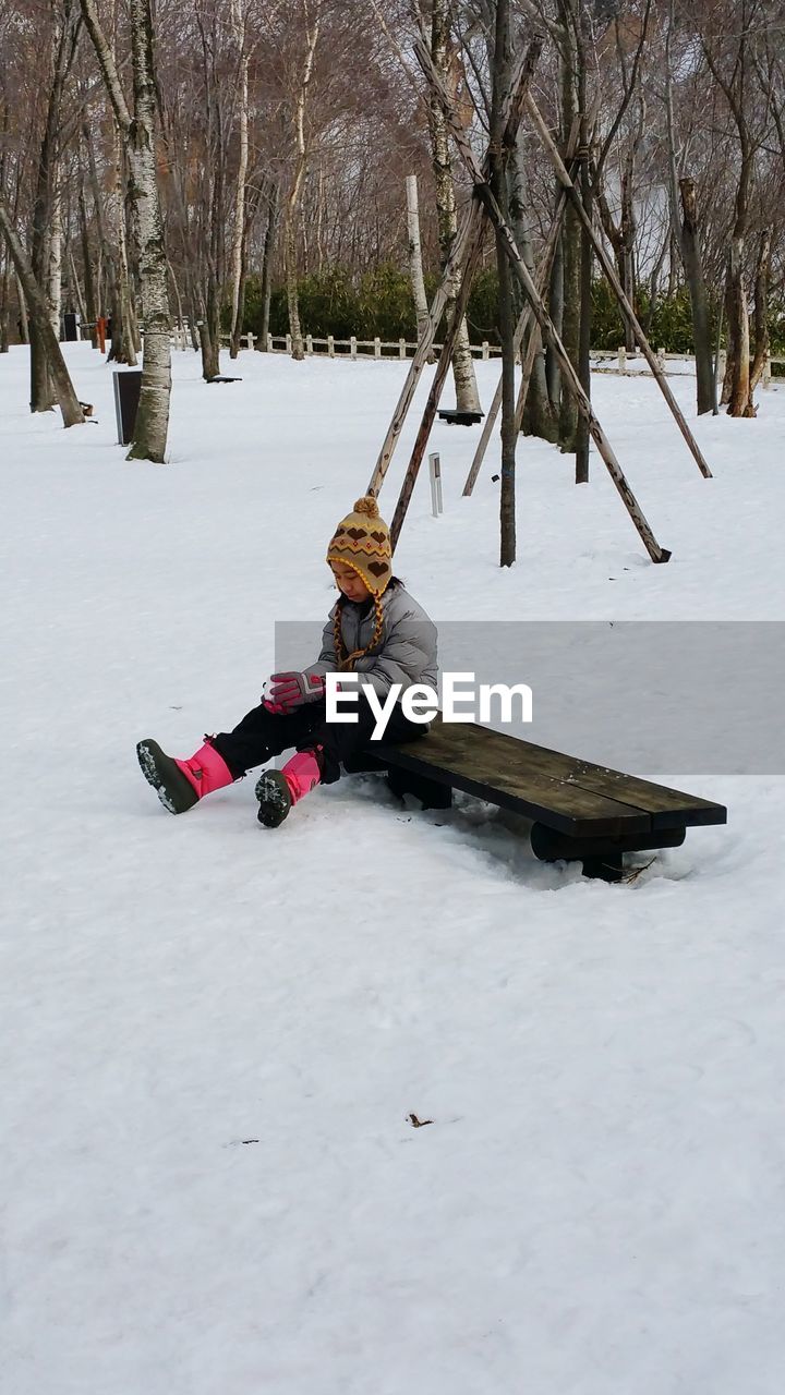 Girl sitting on wood at snow covered field during winter