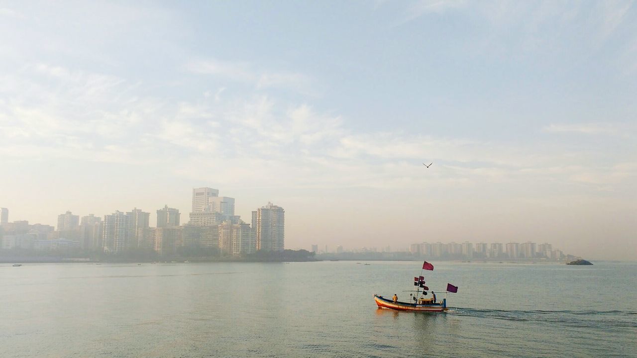 Boat moving in river by city against sky