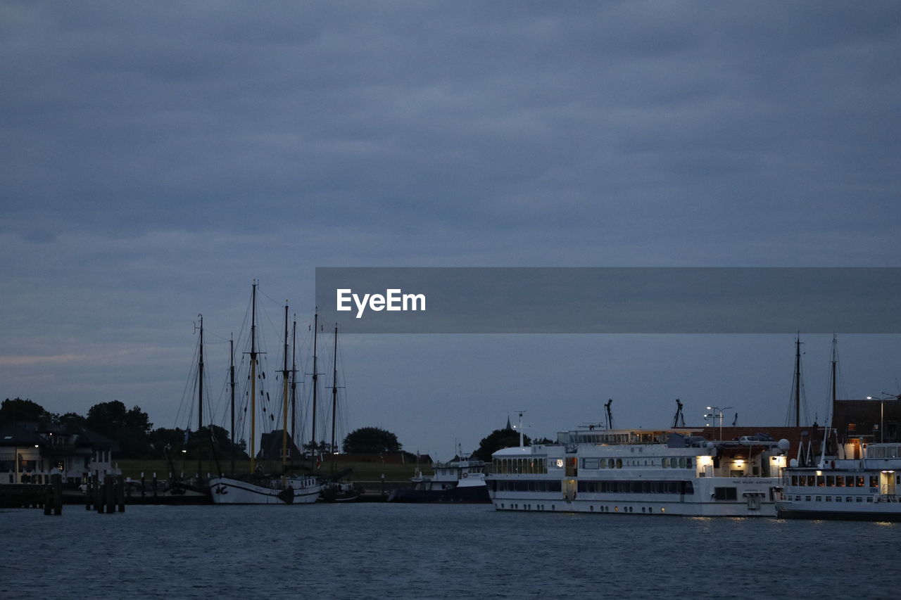 Sailboats in sea by buildings against sky at dusk