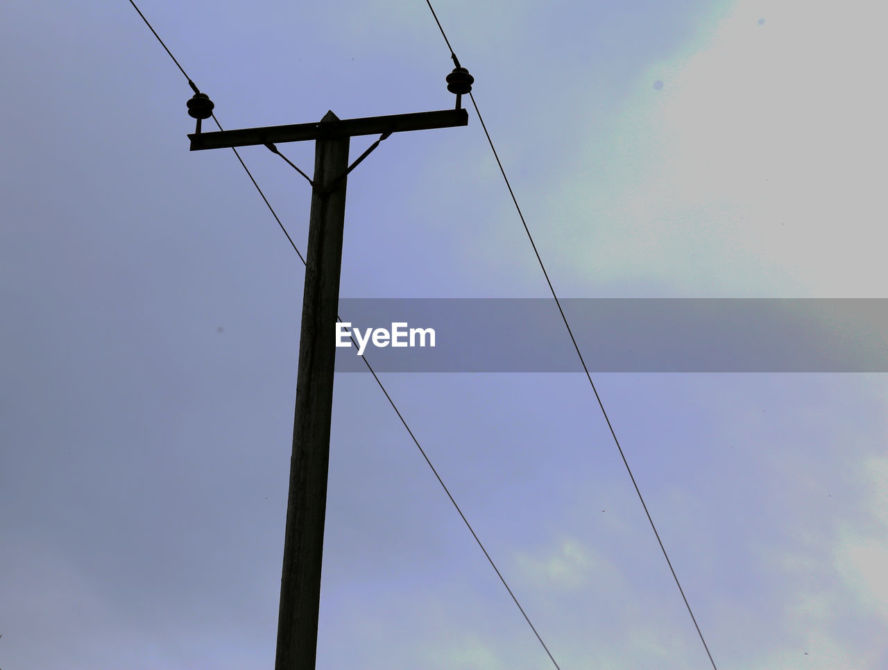 Low angle view of electricity pylon against cloudy sky