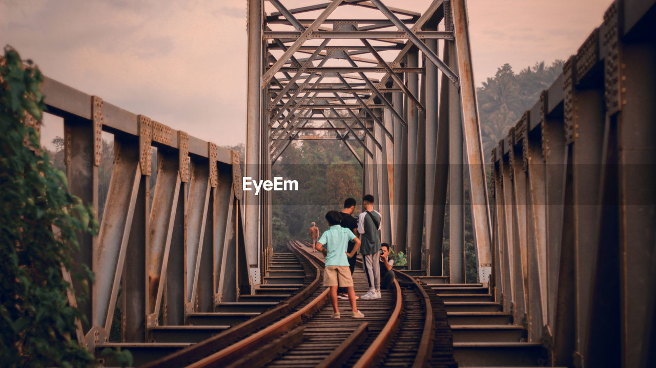 People standing on railway bridge against sky