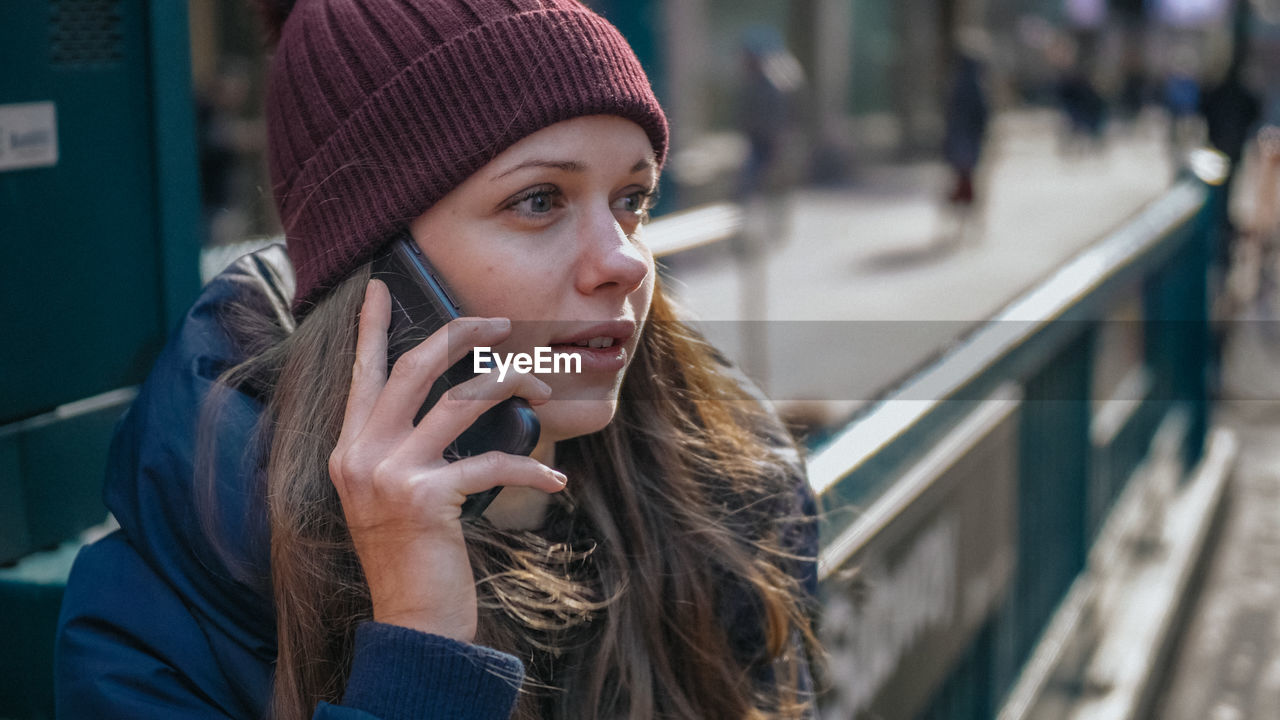 PORTRAIT OF YOUNG WOMAN USING PHONE IN CITY