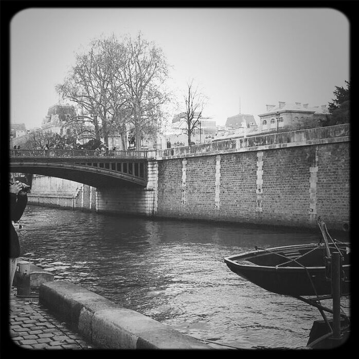 Boat moored on river over bridge by wall against sky