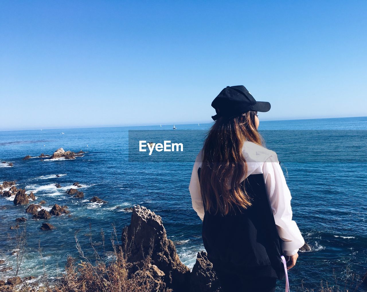 Rear view of woman standing by sea against clear sky