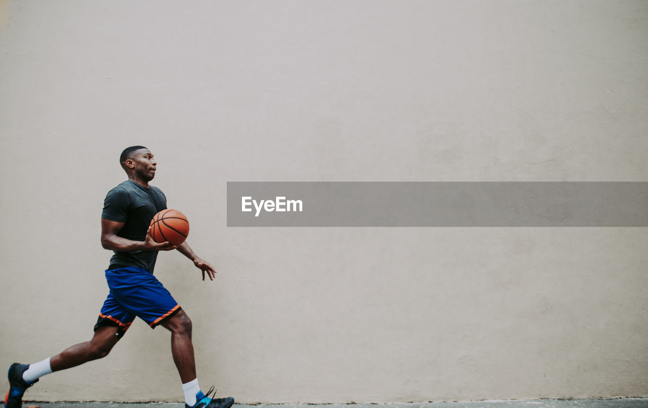 Young man playing basketball against wall