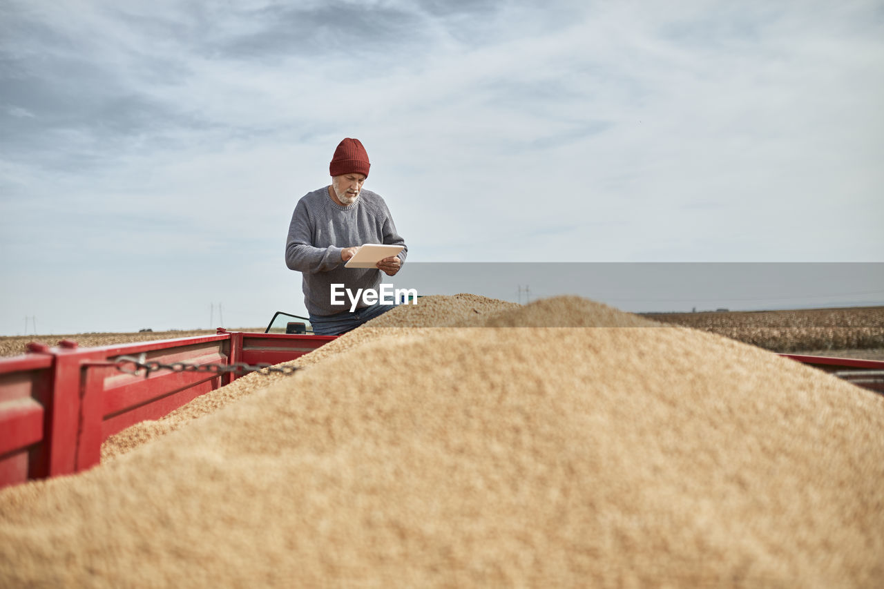 Farmer using digital tablet while standing on tractor against clear sky