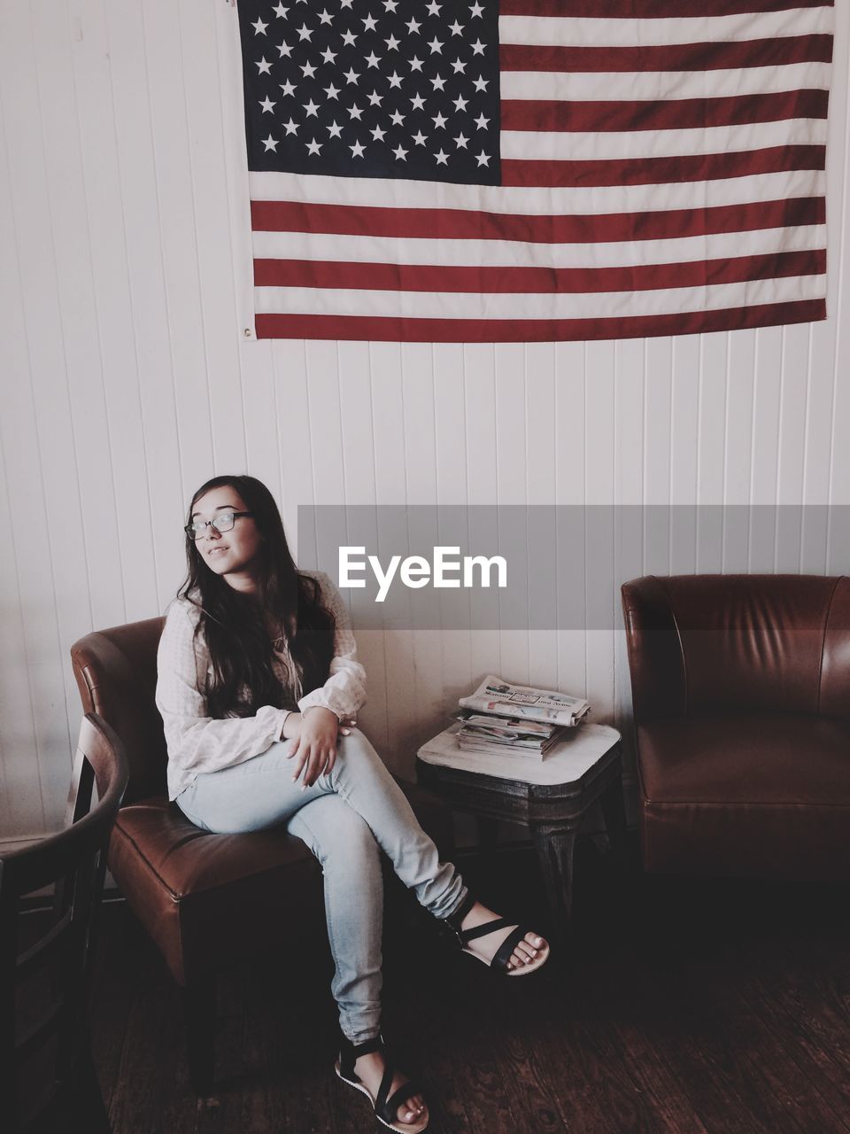 Full length of woman sitting on chair against american flag on wall at home