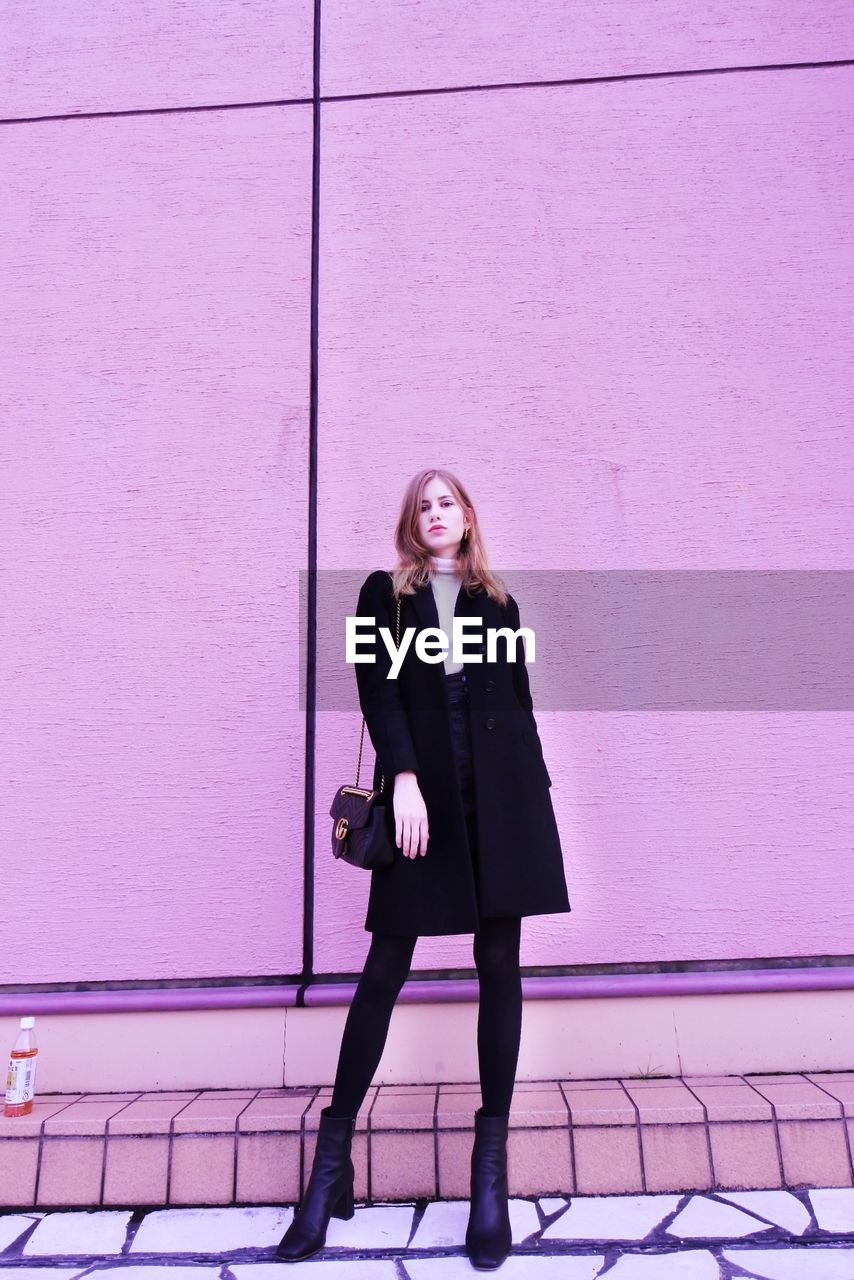 Full length portrait of woman standing against pink wall