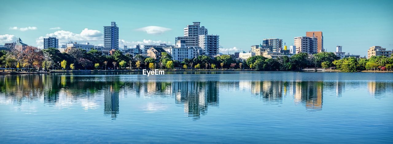 Reflection of buildings in lake against sky in city