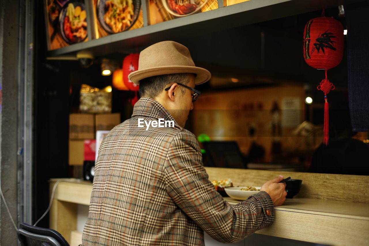 Rear view of boy wearing hat eating food at cafe