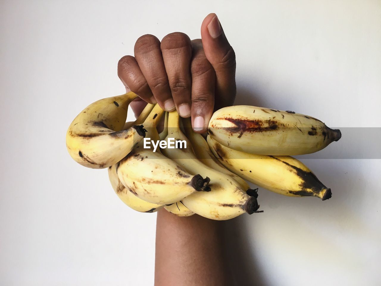 CLOSE-UP OF HAND HOLDING BANANA OVER WHITE BACKGROUND