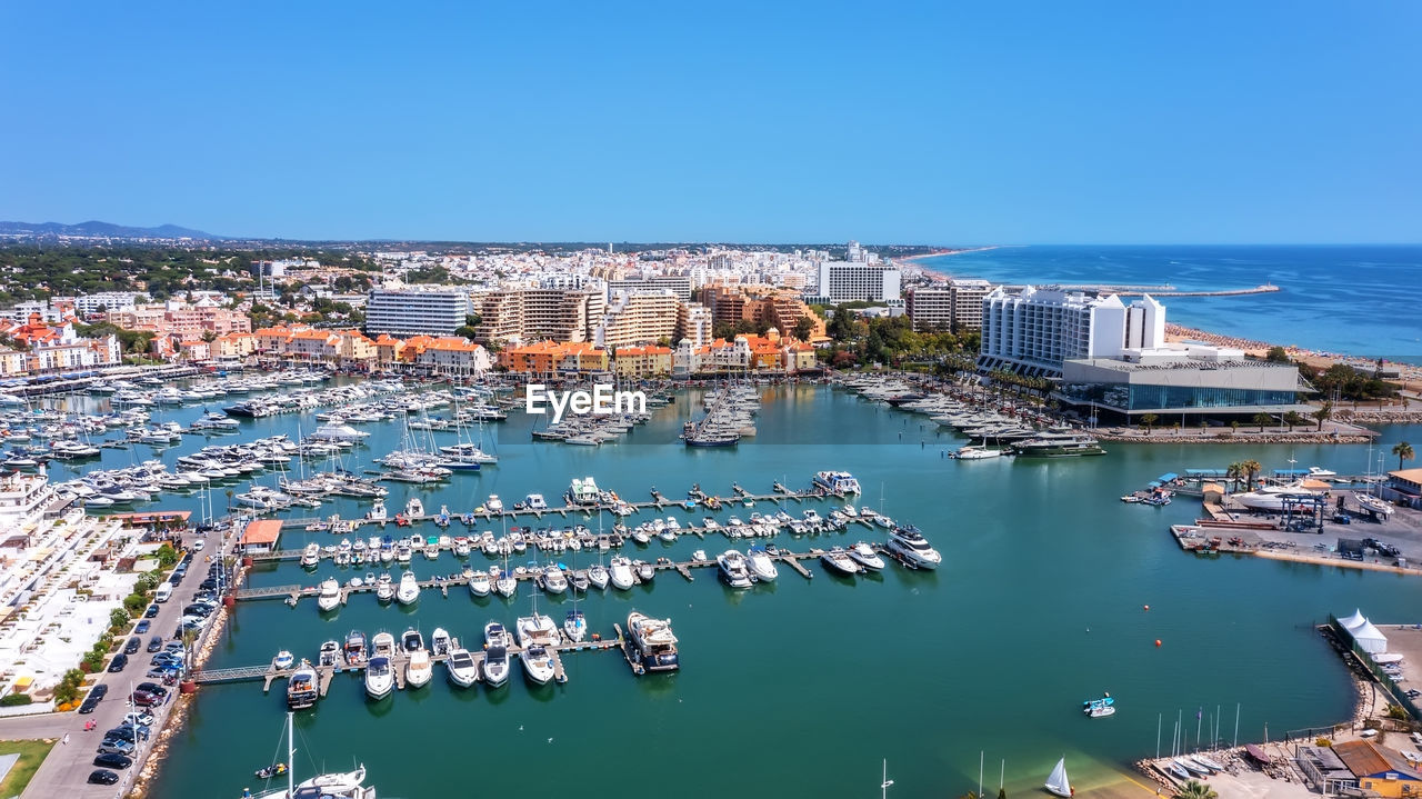 HIGH ANGLE VIEW OF CITY BY SEA AGAINST CLEAR SKY