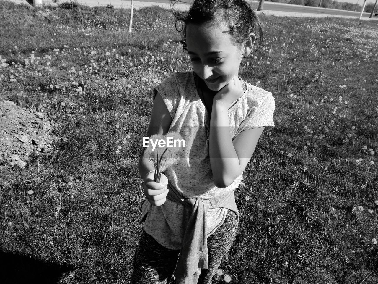 Smiling girl holding dandelions while standing on field