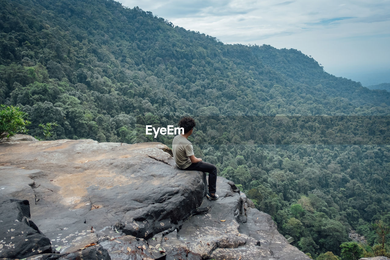 WOMAN SITTING ON ROCK LOOKING AT MOUNTAIN