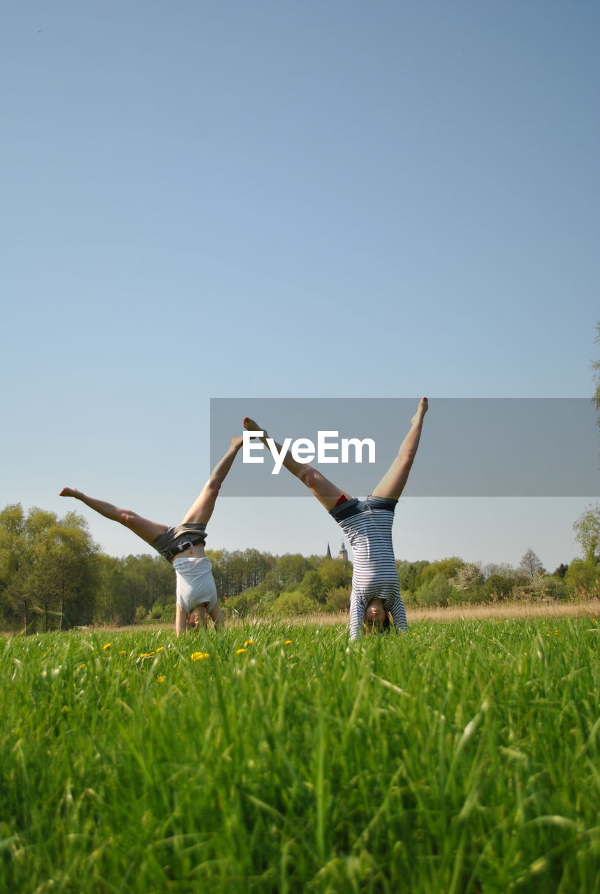 Friends doing handstand on field against sky