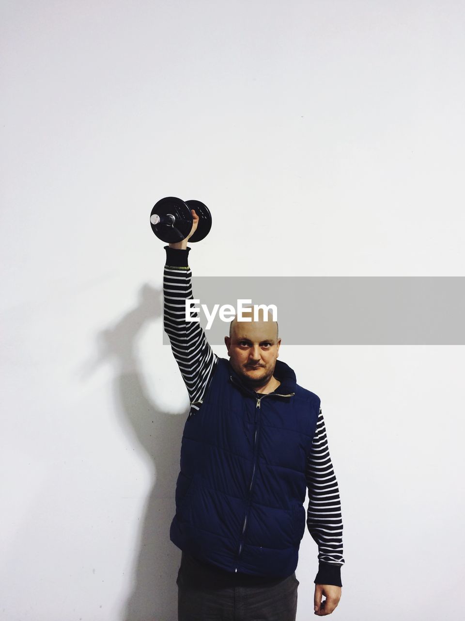 Portrait of mid adult man exercising with dumbbell over white background