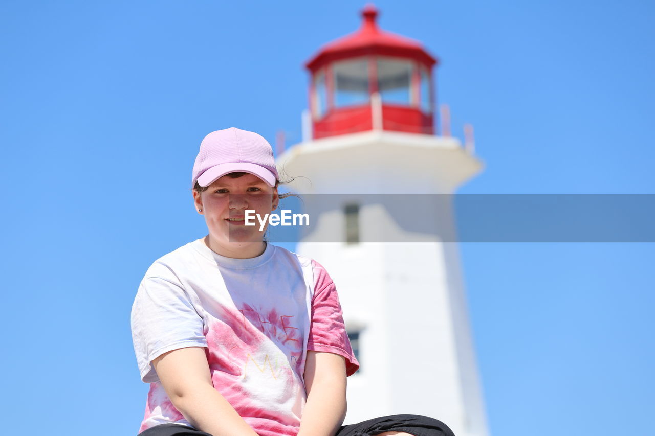Portrait of smiling teenage girl sitting against lighthouse