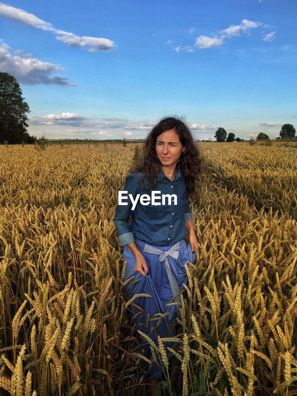 Young woman walking amidst crops on field against sky