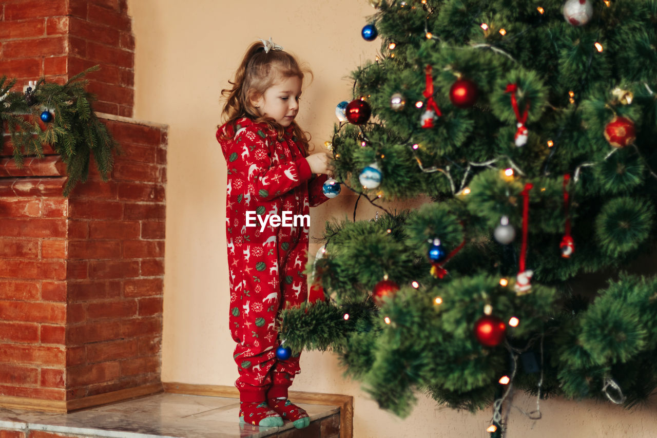 Adorable little girl decorating a christmas tree with colorful glass baubles at home