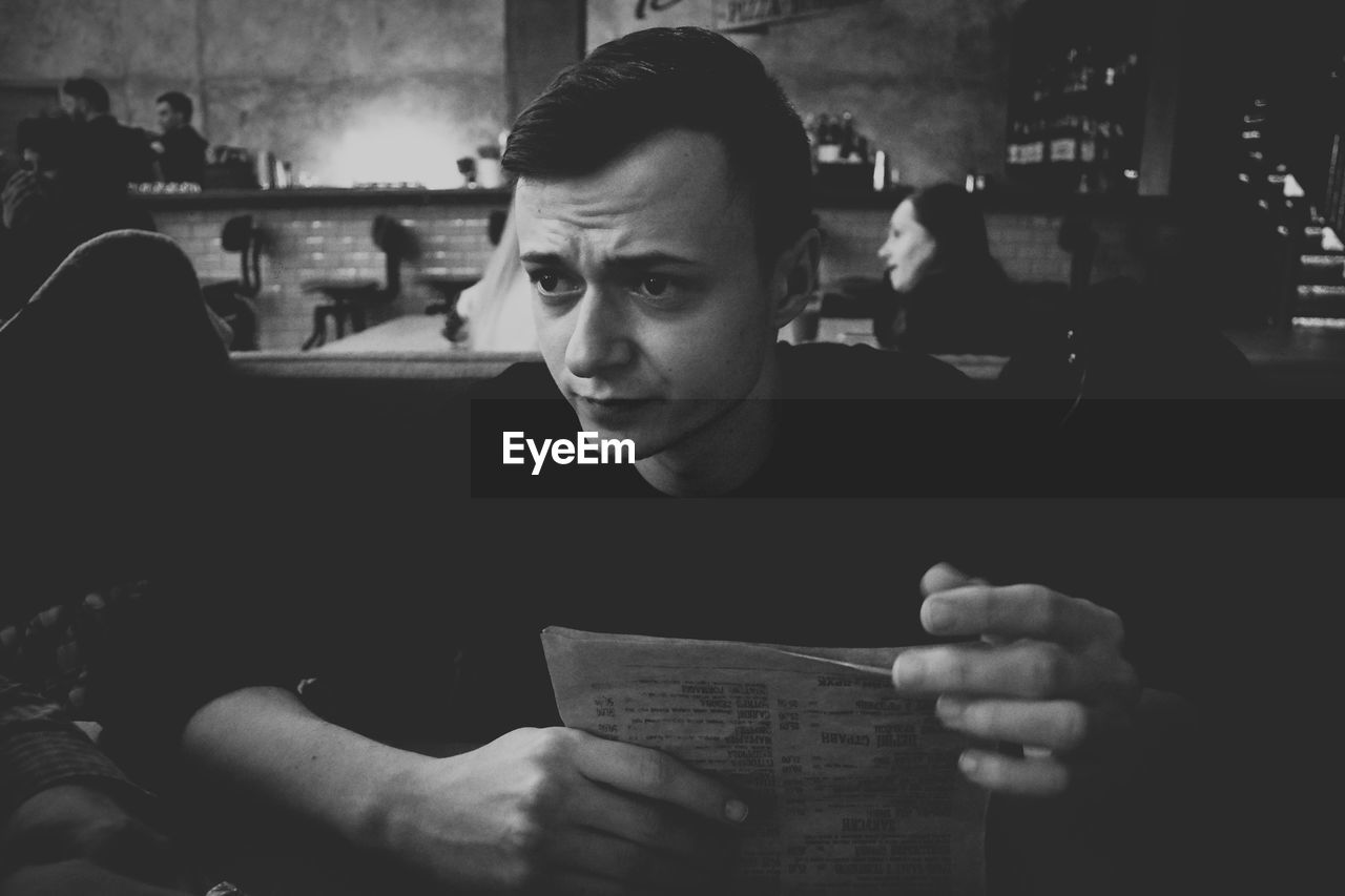 Young man with menu looking away while sitting in cafe