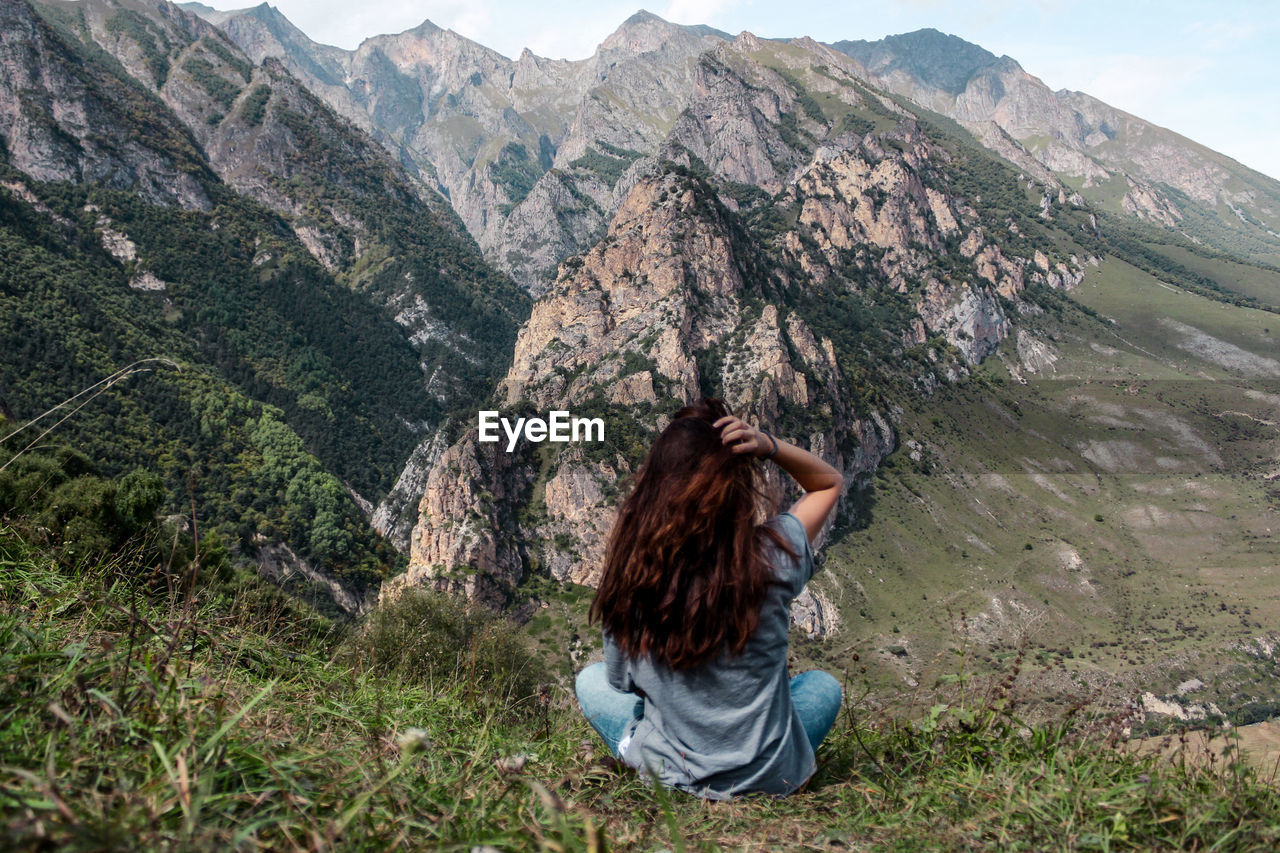 REAR VIEW OF WOMAN SITTING ON LANDSCAPE