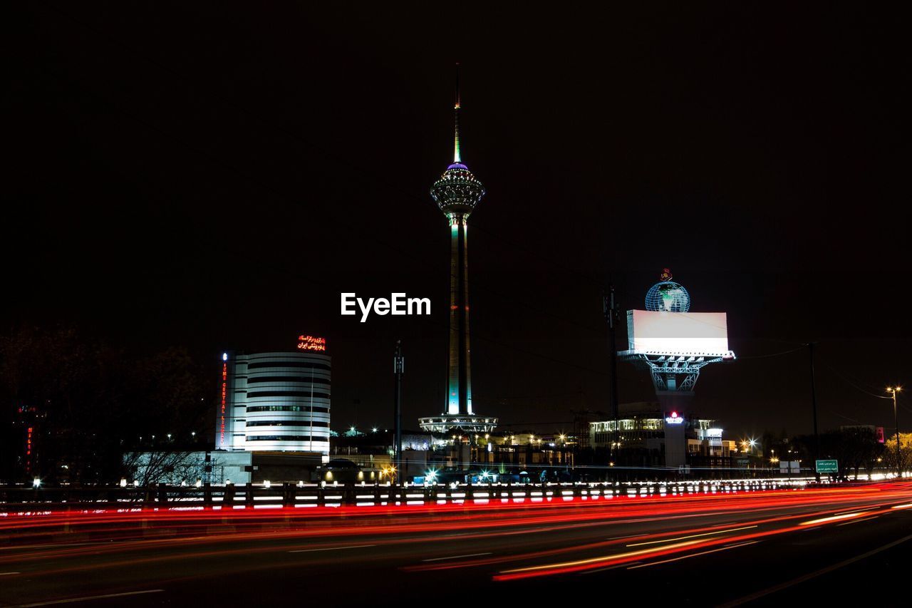 Light trails on road with milad tower against sky in city at night