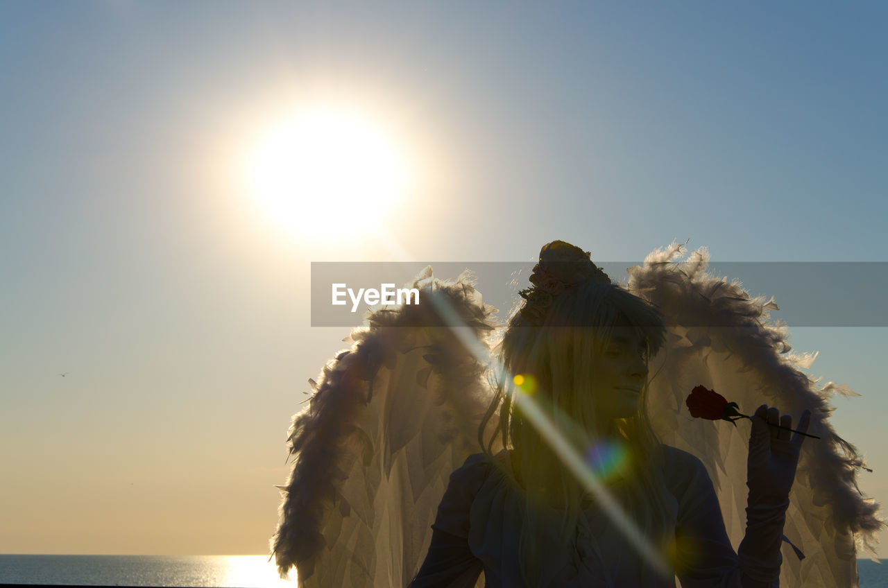Young woman in fairy costume standing at beach against sky during sunset