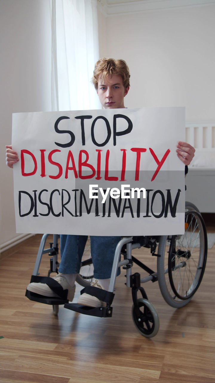 Portrait of young man holding poster sitting on wheelchair