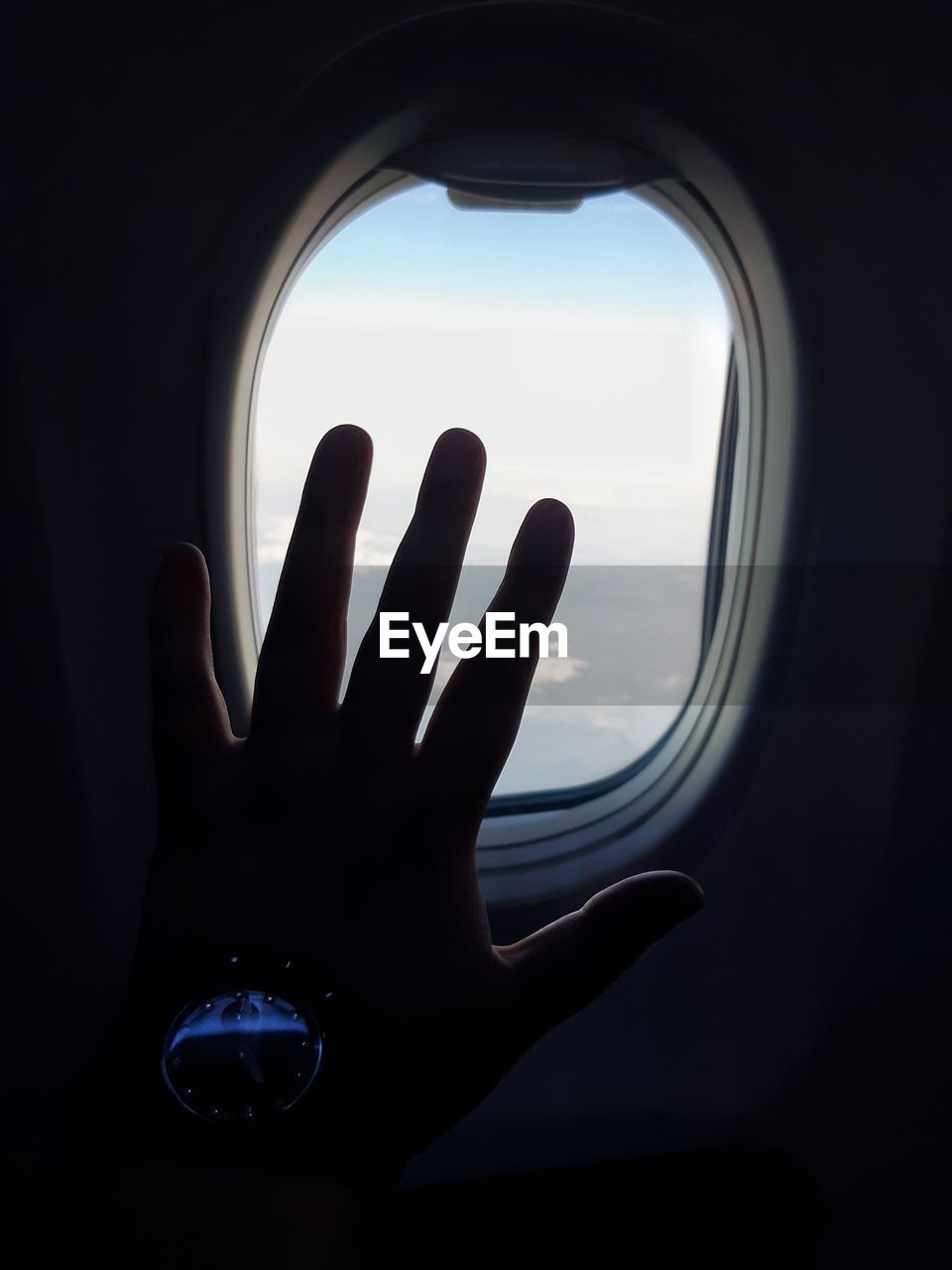 CROPPED IMAGE OF HAND ON WINDOW AGAINST SKY