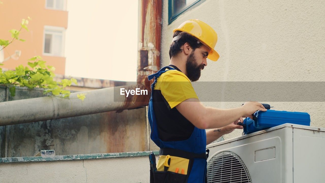 side view of man using mobile phone while standing against wall