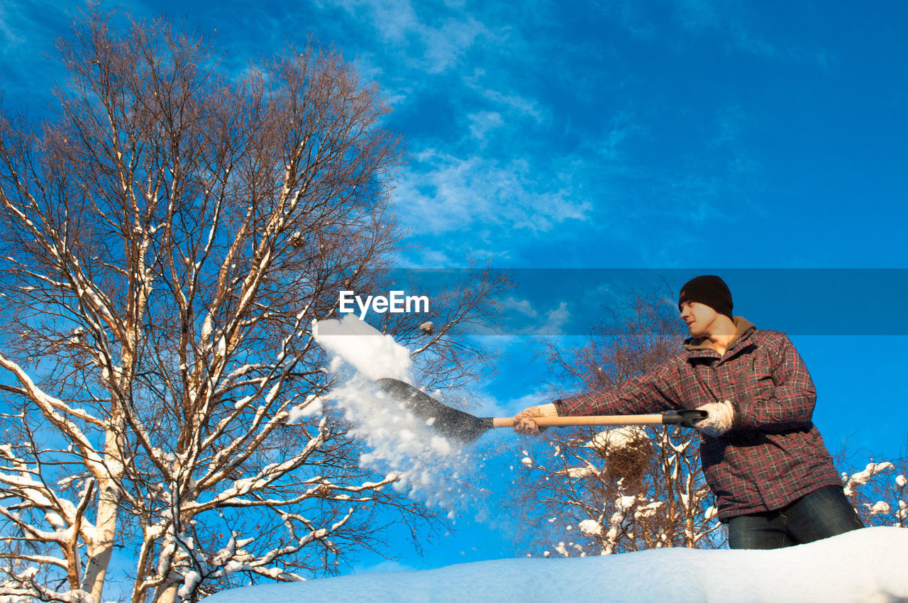 Low angle view of man shoveling snow against blue sky