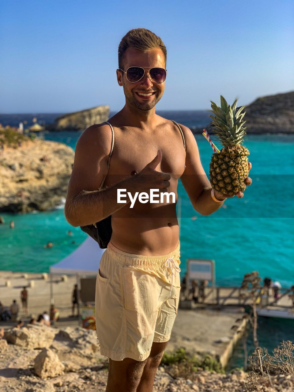 Young man gesturing while holding pineapple at beach