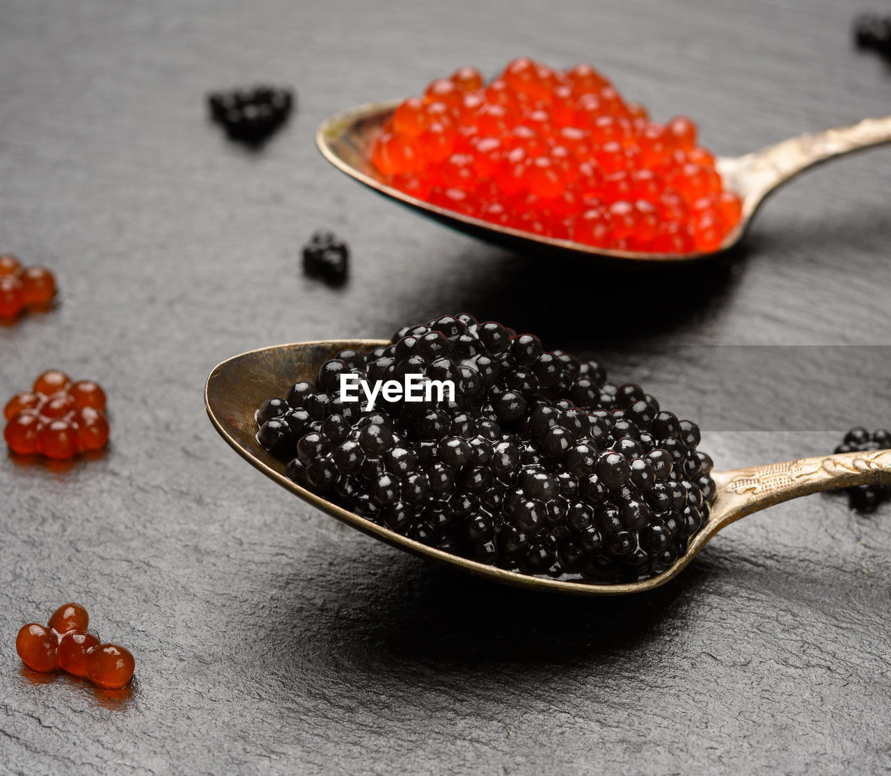 Grainy caviar of paddlefish fish and red chum salmon caviar in a spoon, black background, close up