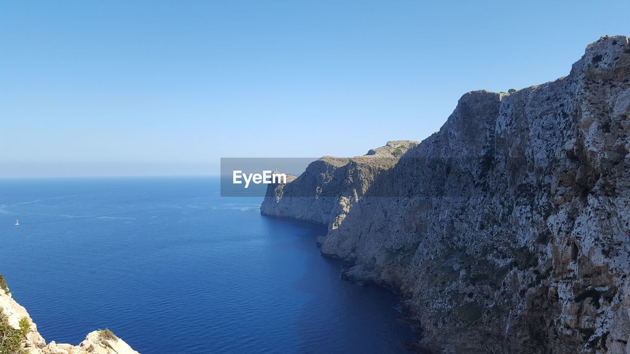 Rock formations by sea against clear blue sky