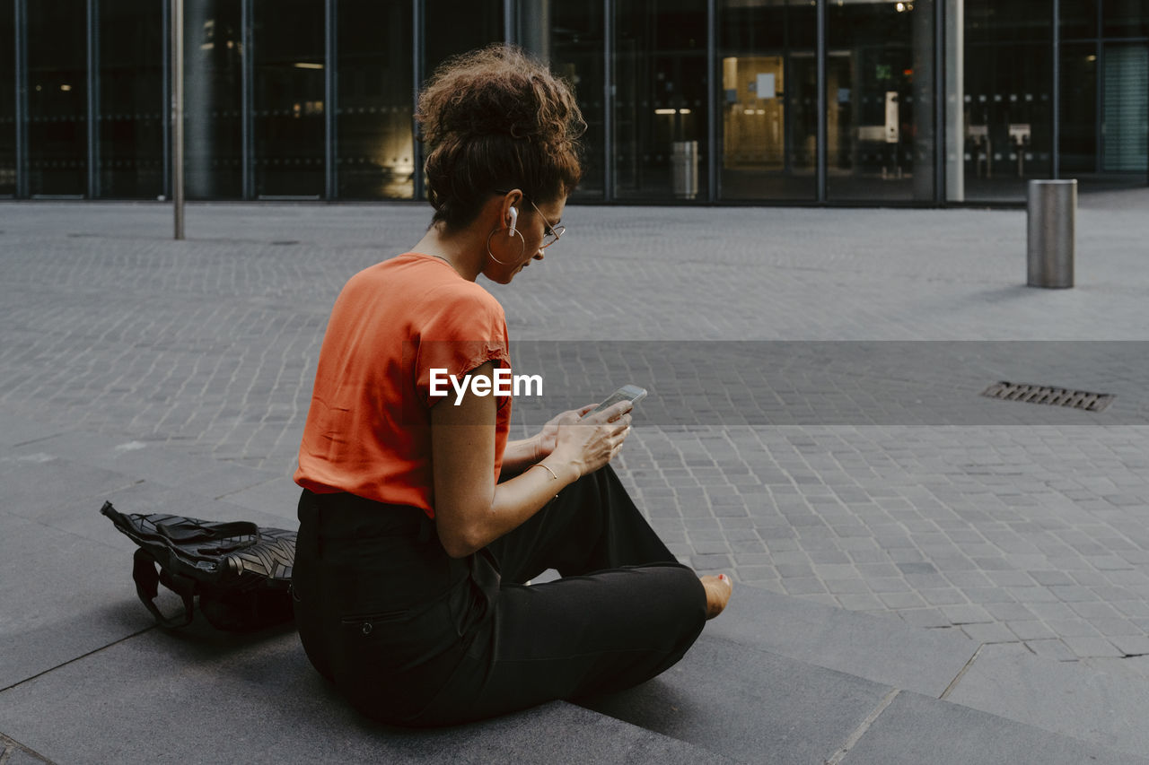 Businesswoman using smart phone while sitting on steps in city