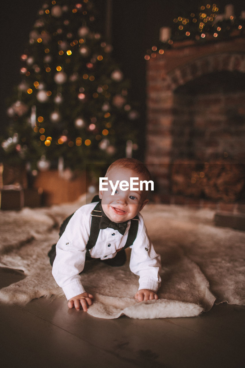 Cute baby boy crawling on floor against christmas tree at home