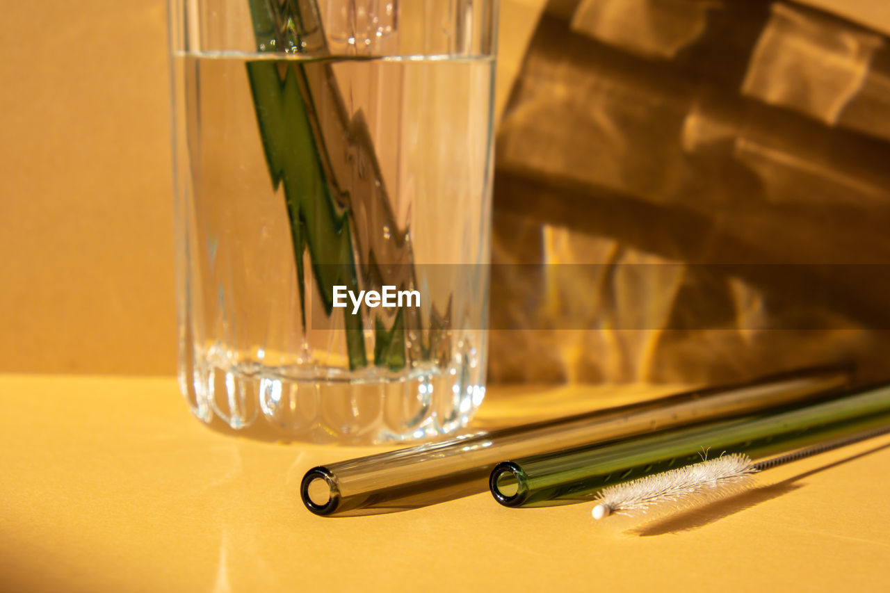 Reusable glass straws in glass with water on beige neutral background eco-friendly drinking straw