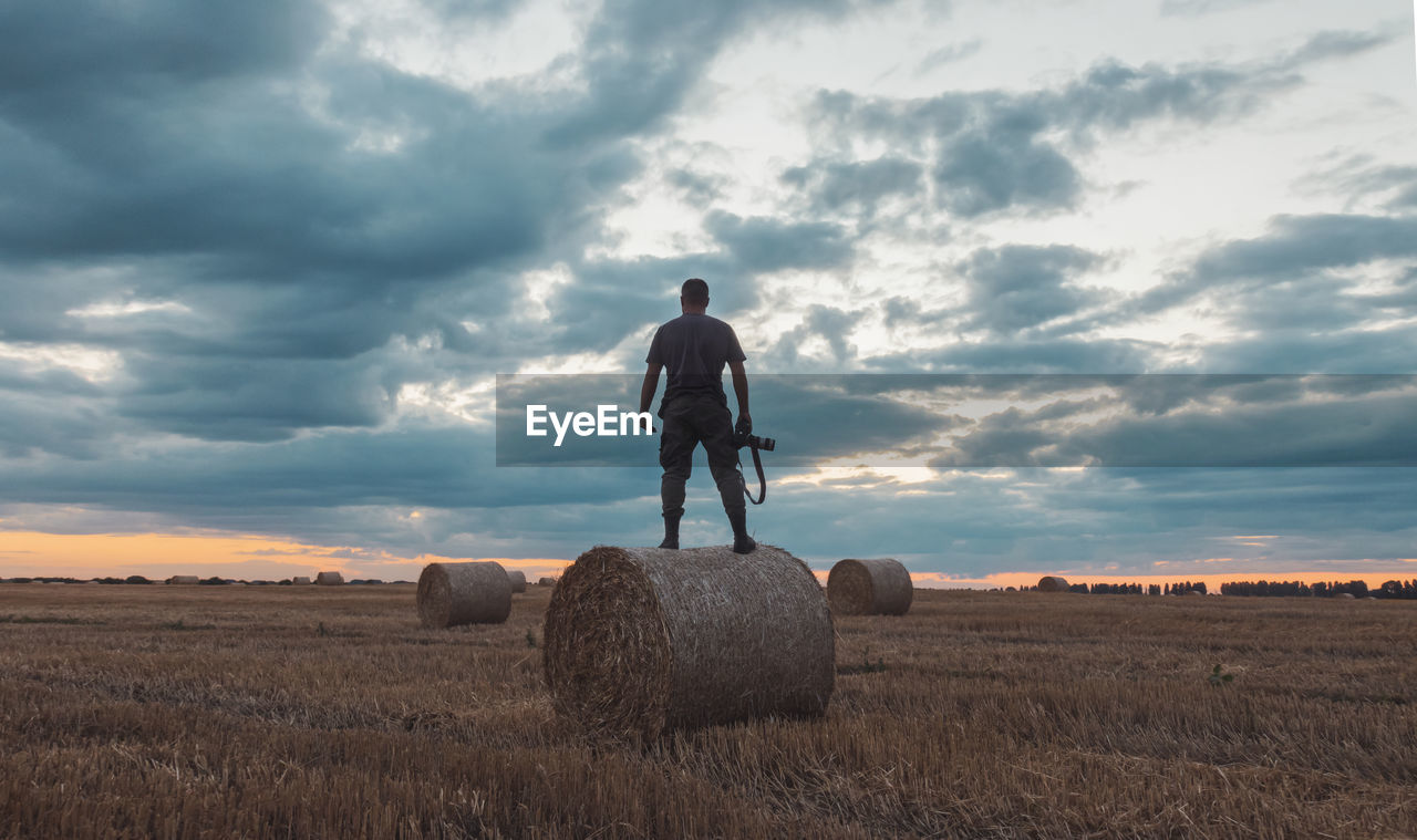 FULL LENGTH OF MAN WITH HAY BALES ON FIELD